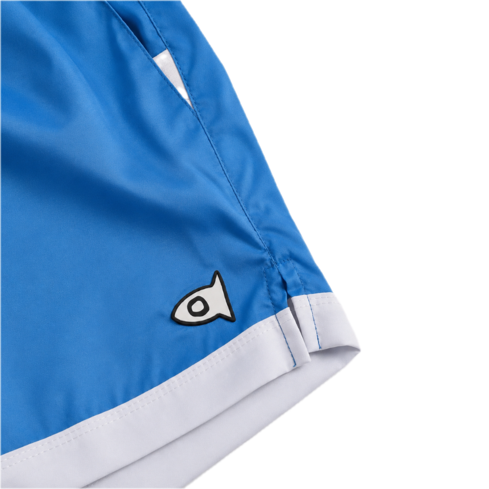 Close-up of blue athletic shorts with a white hem stripe and a small black-and-white fish logo patch, shown on a white background.