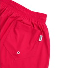 Close-up of bright red swim trunks showing an elastic waistband, a side pocket with a metal grommet, and a small white brand tag reading 'Fishi'.